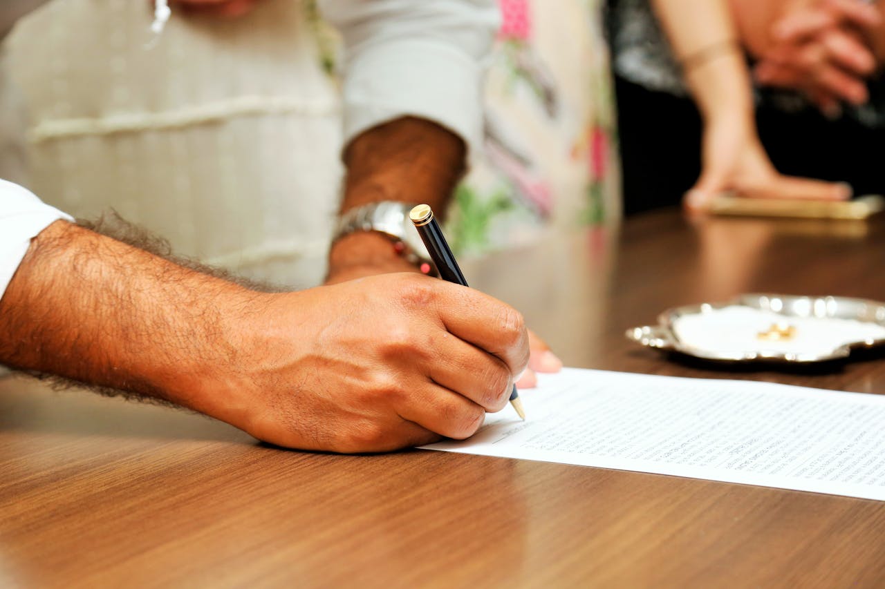services-03 Close-up view of a person signing an important document with a pen on a wooden table.