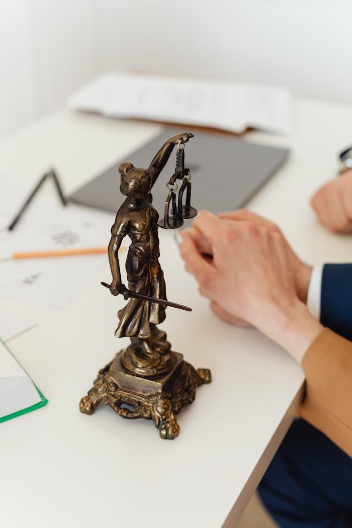 services-01 Bronze Lady Justice statue on a white office desk with hands in the background. Symbol of law and fairness.