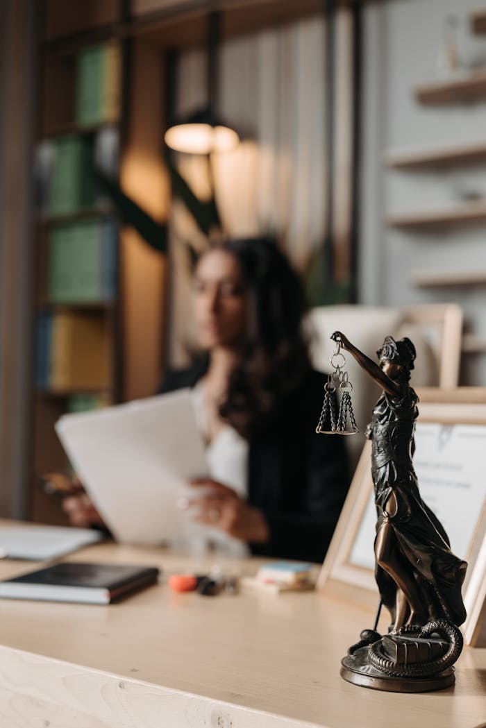 our-journey-01 Close-up of a justice figurine on desk with blurred female lawyer in office setting.